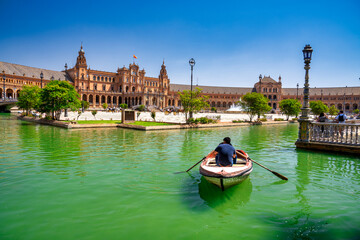 Obraz premium Sevilla, Spain - April 10, 2023: Several boats with people rowing at leisure on the lake of Plaza de Espana with buildings in the background
