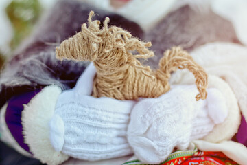 hand in white mittens hold the decor horse on a background of snow