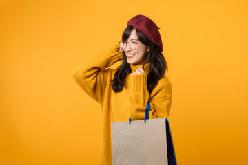 A happy young woman in a red beret and yellow sweater enjoys her shopping spree, holding a paper...