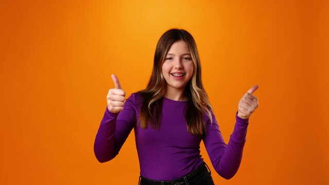 Happy smiling teen girl showing thumbs up gesture against orange background