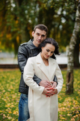 A man hugs his pregnant wife. A man in a black leather jacket hugs a woman in a white coat