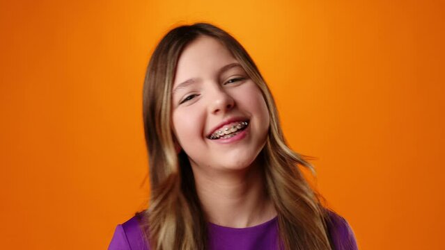Teenager girl smiling with braces on her teeth against orange background