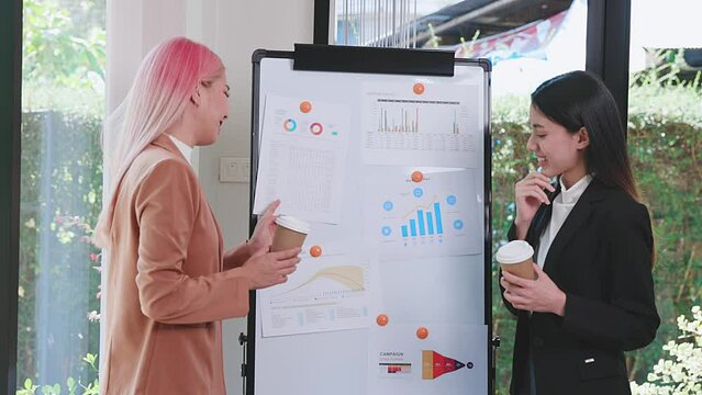 Two Businesswomen making a presentation at work in front of colleague. Businesswoman coach mentor explain graph chart on flipchart corporate group workshop training in meeting room.