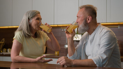 Happy middle-aged old senior couple Caucasian family woman and man drinking orange juice at kitchen home cheerful talk spouses retired wife and husband drink fresh fruit healthy nutrition healthcare - Powered by Adobe