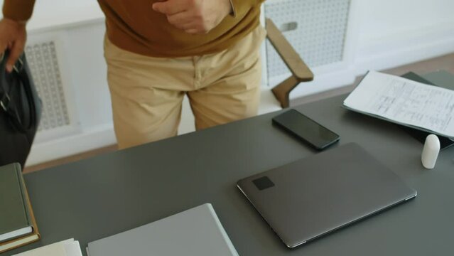 Cropped high angle shot of male therapist taking off his gadgets from leather briefcase, sitting at desk and using laptop while getting started with workday