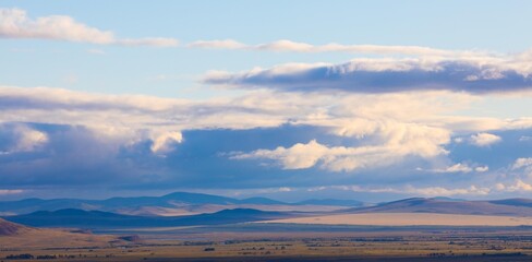 Panoramic landscape with Khakassia steppe under sky with heavy clouds at early autumn day in Siberia, Russia. Cloud shadows lie on the ground