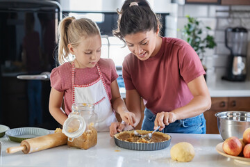 Beautiful happy mother and daughter preparing an apple pie at home kitchen. Autumn fun family activities
