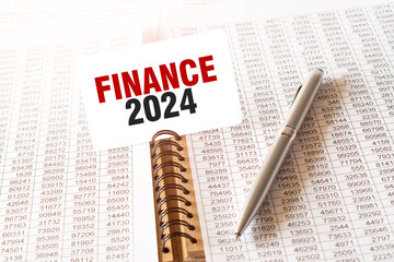 Text FINANCE 2024 on paper card, pen, financial documentation on table