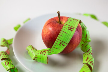 red apple and measuring tape on a plate as a symbol of healthy eating.