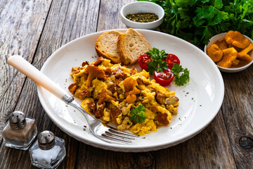 Scrambled eggs with chanterelle mushrooms with fresh tomato salad on wooden table  © Jacek Chabraszewski