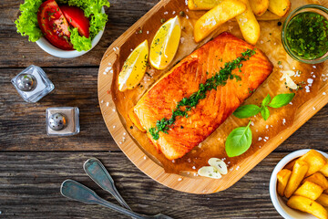 Seared salmon steak with french fries and lemon served on wooden table
