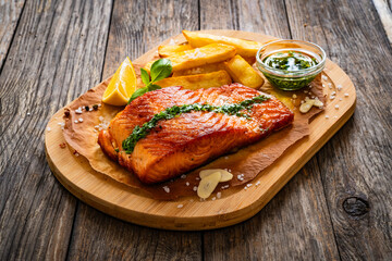 Seared salmon steak with french fries and lemon served on wooden table
