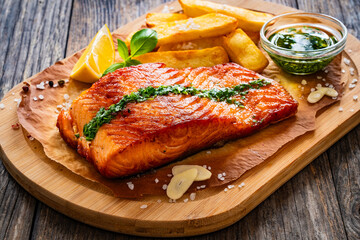 Seared salmon steak with french fries and lemon served on wooden table
