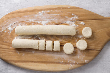 Wooden board with raw cottage cheese gnocchi on a light gray background, top view. Cooking stage