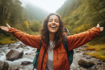 A woman stands in front of a river, with her arms outstretched. This image captures the beauty and serenity of nature. Perfect for a variety of uses, such as wellness blogs, travel websites, and outdo