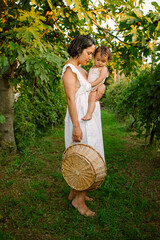 Young mother with her baby girl walking through a vineyard in summer playing and tasting fruits before the harvest at sunset. Summer nature. Smiling happy child and family. Fun family and relax