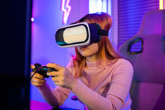 Excited woman virtual playing gamepad controller she very determined at home, Gamer in VR headset glasses exploring metaverse play video game online with joystick on computer neon lights