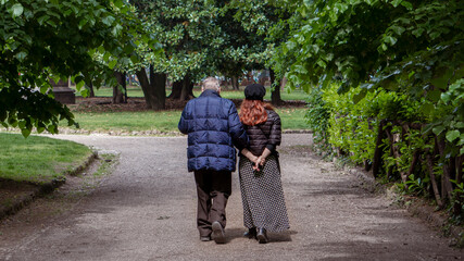 Elderly couple walks with their backs turned.Senior lovers hiking for a healthy lifestyle in the forest. Old couple in public park.