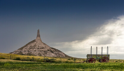 Chimney Rock in Nebraska, USA and a replica of a covered wagon with a storm approaching.