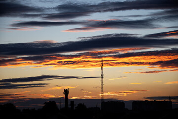 Naklejka premium Dark, clear silhouettes of roofs of houses with chimneys and pipes in rays of setting sun. Sunset in city. Silhouette City landscape in backlight of sunset. Landscape Sky.