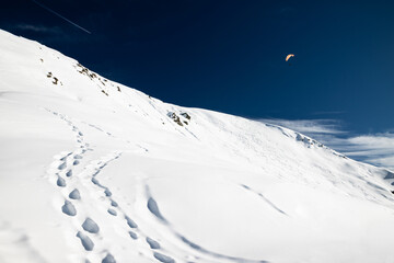 Foot steps on fresh snow and clear sky with one paraglider