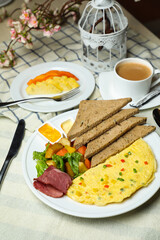 Stuffed Omelette with bown bread, meat, vegetable salad include tomato, potato, lettuce leaf and carrot with tea, coffee, and sweet melon served on food table top view healthy breakfast