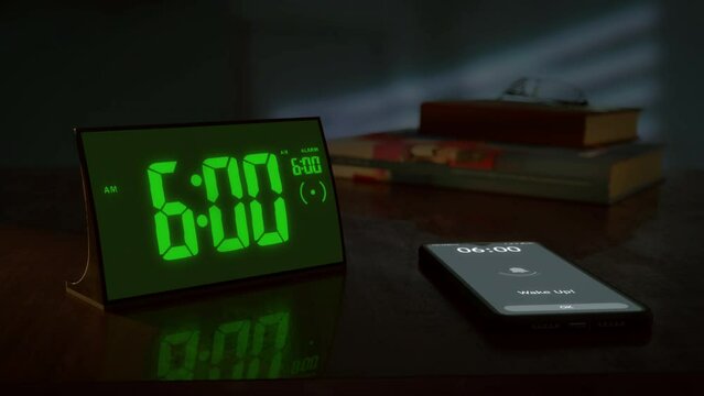 Digital alarm clock with green clockface and the smartphone waking up at 6 AM. The numbers on the clock screen changes from 5:59 no 6:00 AM. And the alarm goes off on the phone. Close up view.