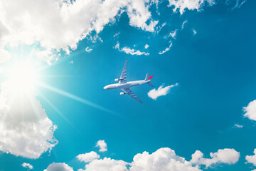 Airplane in the blue sky with clouds from below, high flying passenger plane. jet plane flying overhead diagonally in sky with sunlight. Bottom view