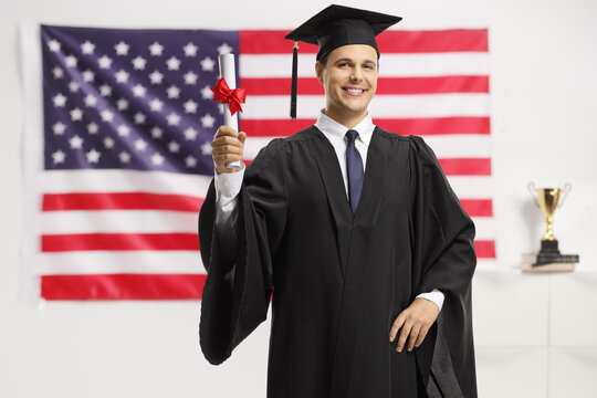 Young man in a graduation gown and cap holding a diploma in front of a USA flag