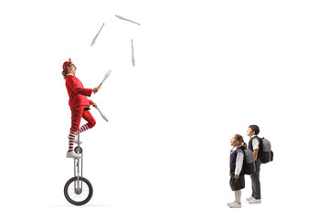 Schoolchildren watching an acrobat riding a giraffe unicycle and juggling