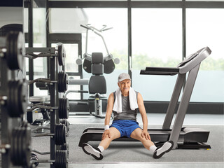 Fototapeta na wymiar Tired elderly man sitting on a treadmill at the gym