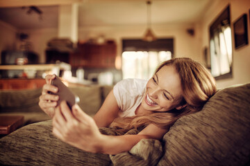 Young Caucasian woman using her smartphone on the couch in the living room at home