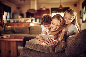 Happy young mother and her children using a smartphone on the couch in the living room at home