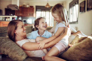 Young mother playing with her children on the couch in the living room at home