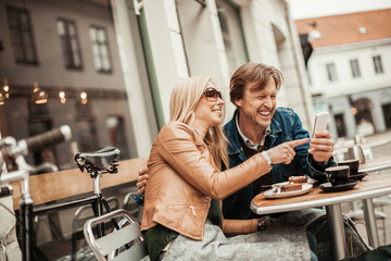 Middle aged Caucasian couple using a smartphone while having coffee and desserts in a outdoor café in the city