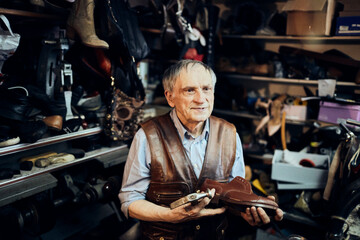 Senior male cobbler restoring a shoe in his old workshop in the city