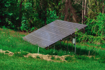 A dark blue solar panel, comprising smaller panels, positioned at an angle in a lush green field, supported by sturdy metal poles. Trees form a natural backdrop to this eco-friendly energy source.