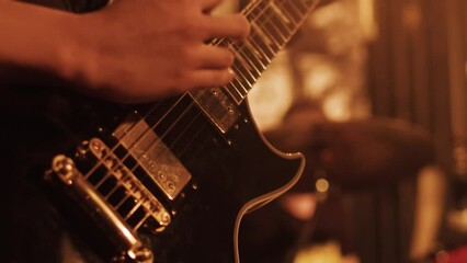 Guitarist playing the melody on a guitar during the performance on a stage with bright lights close up. Musician performing a rock song
