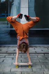 Tuinposter Parkour trick on skateboard. Teen girl stands on her hands on skateboard outdoors. © meteoritka