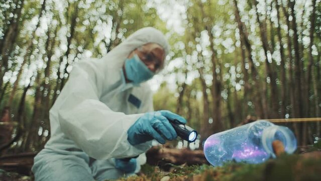 Woman forensic police investigator checking for fingerprints on an bottle on a crime scene in the woods