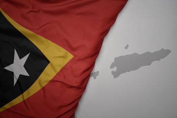 big waving national colorful flag and map of east timor on the gray background.