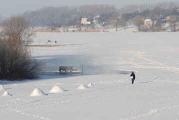 Winter landscape on a snowy lake and a fisherman walking in the distance, winter fishing.