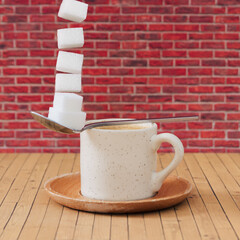 Creative composition made of cup of coffee, spoon and flying sugar cubes against red brick wall...