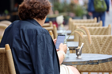 Woman sitting with smartphone in hands on city street at the cafe table