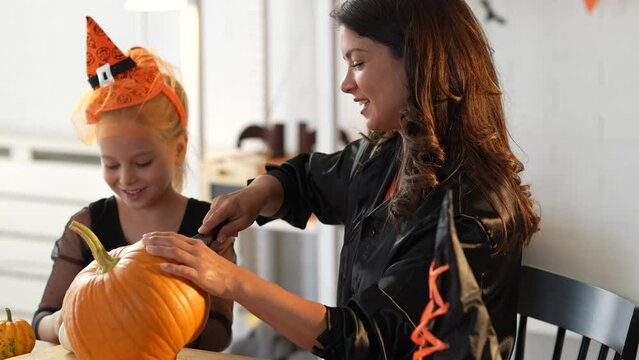 Video of mother and daughter carving pumpkin for Halloween autumn holidays. Mother and daughter in costumes having fun.