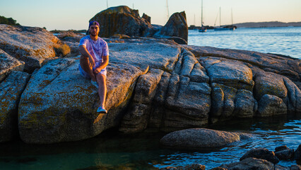 caucasian man watching the horizon sitting on the rocks of the sea