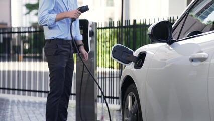 Progressive businessman install charger plug from charging station to his electric car before...