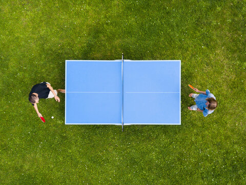 Aerial view people playing ping pong match outdoor. Top view two boys playing table tennis on a green grass lawn. Aerial view outdoor sport