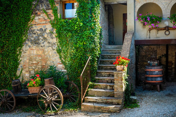 A peaceful Tuscany farmyard with stairs leading up into the house, a wine crushing barrel, and a...