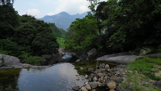 Captivating aerial footage of a drone hovering over a river cascading from a waterfall in a rural village nestled amidst mountainous forests, perfect for nature and travel